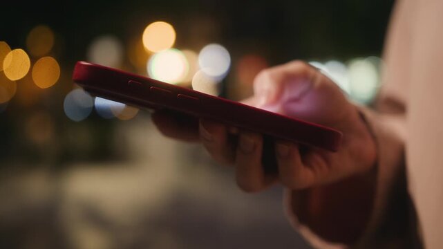 A girl against the backdrop of glowing storefronts and the lights of a night city uses her phone to order a taxi and spends time on social media. High quality 4k footage