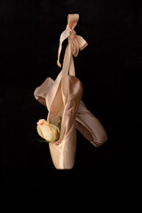 ballet slippers with rose hanging on black background © JM