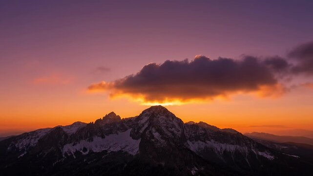 Dramatic mountain range at sunset with a single cloud illuminated orange