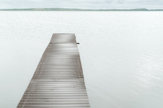 Canada, SK, Lloydminster, Manitou Lake.  Weathered wooden dock juts out into the still lake.