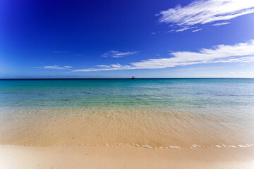 Obraz premium Pristine sandy beach with crystal-clear turquoise water and gentle waves under a deep blue sky in the Florida Keys, featuring a distant boat on the horizon and a serene tropical atmosphere