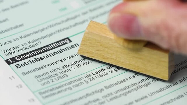 Ein Holzstempel mit dem Abdruck "Pr&uuml;fung" wird auf ein Steuerformular f&uuml;r Gewinnermittlung und Betriebseinnahmen gedr&uuml;ckt - FOTOMONTAGE - digital nachbearbeitet
