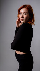 Fototapeta premium Portrait of Stylish Redhead Female Model Against Dark Backdrop in Professional Studio