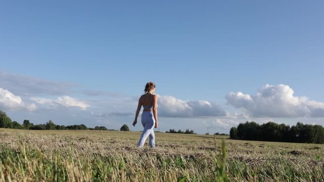 A woman in sportswear walks through a field in a village on a sunny summer day