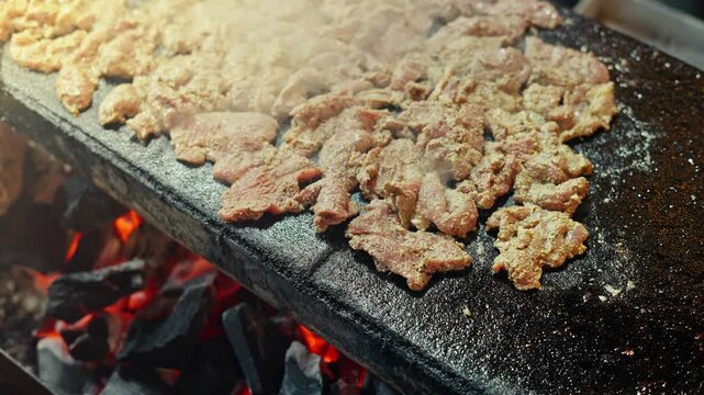 Traditional Hyderabadi Pathar ka Gosh sizzling on a hot stone grill over charcoal fire, a popular street food delicacy during Ramadan in Hyderabad, India.