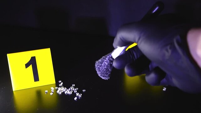 Close view of forensic investigator dusting diamonds for fingerprints beside numbered evidence marker during crime scene examination.