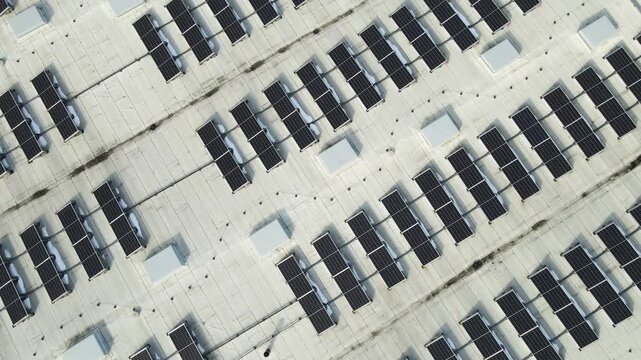 Drone view of rooftop photovoltaic array on modern industrial warehouse with melting spring snow and clean energy infrastructure.