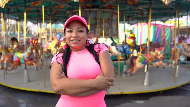 Latin woman entrepreneur smiling, standing next to colorful carousel horses at an amusement park