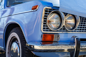 Fototapeta premium Close-up of a blue vintage car front: headlights, chrome grille and retro whitewall tires on a cobblestone road.