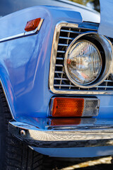 Fototapeta premium Close-up of a blue vintage car front: headlights, chrome grille and retro whitewall tires on a cobblestone road.