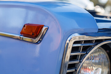 Close-up of a blue vintage car front: headlights, chrome grille and retro whitewall tires on a...
