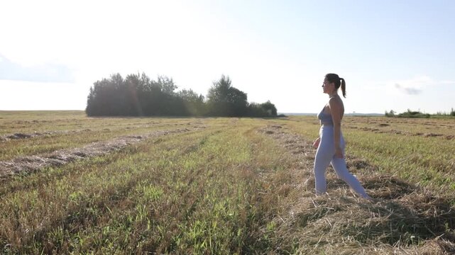 A woman in sportswear walks through a field in a village on a sunny summer day