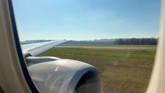 View from an airplane window during takeoff at Zurich Airport on a bright sunny day, runway and landscape visible below.