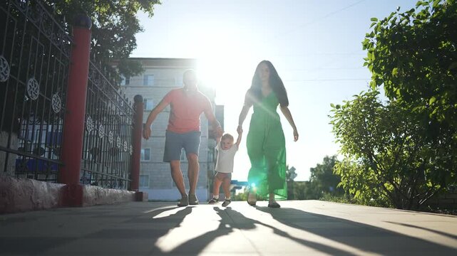 Mom and father help son walk outdoor. Joyful son swings between mom and father receiving support. Family bonding as mom father help son. Parents help son take step. Happy family moment as mom father.