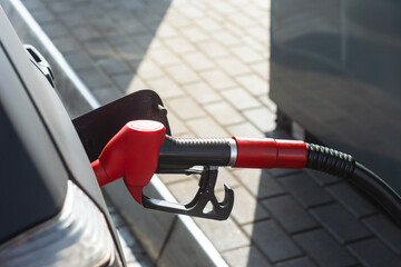 Close-up of a red gasoline nozzle inserted into a black car fuel tank at a modern gas station, with...