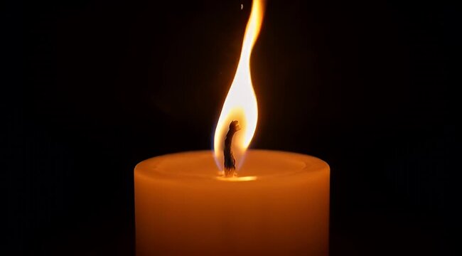 Solitary candle flame casting a warm glow against the darkness of night