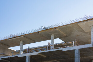 Multi-story reinforced concrete building frame featuring exposed rebar, supporting columns, formwork edges and open floor levels. Raw stage of large-scale construction project. © vadish