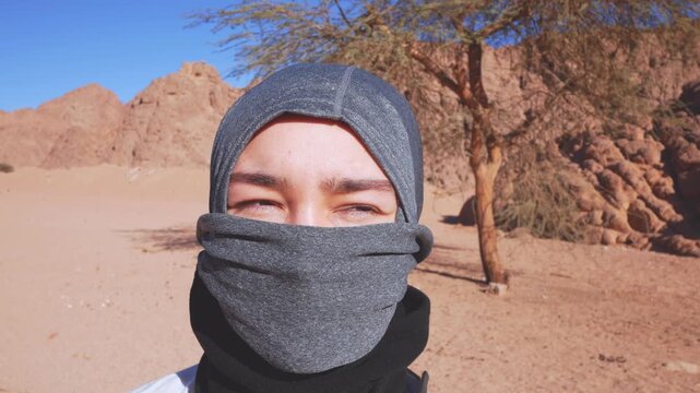 Close-up of a young Bedouin girl wearing a traditional gray niqab face veil and headscarf in the rocky desert.