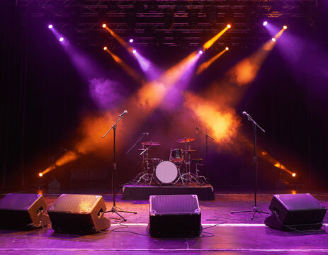 Unoccupied performance platform bathed in striking purple and orange spotlight projections, generating an electrically charged ambiance primed for upcoming musical acts.