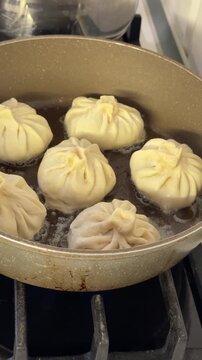 Georgian khinkali dumplings frying in bubbling butter inside nonstick pan on gas stove in home kitchen, vertical cooking video showing handmade dumplings simmering during stovetop meal preparation