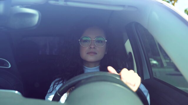 Beautiful happy woman driving a vehicle on sunny day. Female driver beginner practicing driving after getting licence. Caucasian woman with curly hair learning to drive a car. Close up
