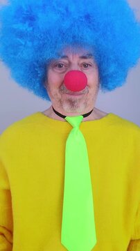 Elderly man dressed as a funny clown is making silly faces on a white background