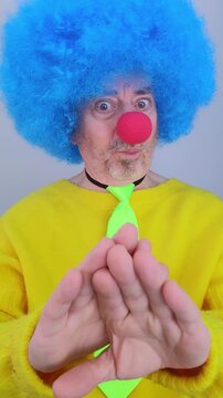 Clown in a blue wig and red nose performing a hand magic trick on a white background