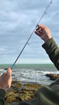 Vertical close up of fisherman hands threading fishing line through rod guides on the beach, shore spinning preparation, angling technique sport fishing hobby, outdoor angling technique 