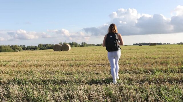 A woman with a backpack in sportswear walks through a field on a bright sunny day on a hike