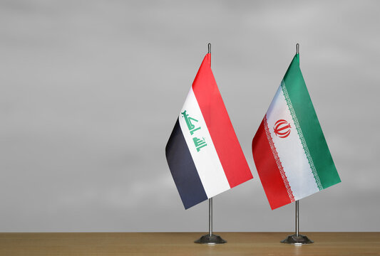 Two table flags of the Iraq and Iran on a blurred gray background