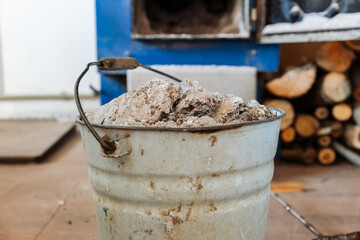 A metal ash bucket stands in front of a blue wood-burning stove with an open door. A stack of chopped firewood lies on the floor. © Paul