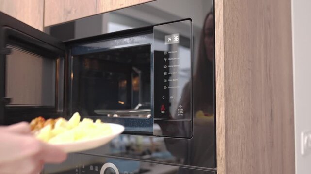 Woman opens built in microwave oven and removes food from inside in kitchen cabinet. Concept of quick home cooking