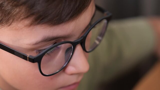 Pupil close up of a young boy wearing black rimmed eyeglasses, deeply focused while reading, highlighting concepts of learning, vision, and concentration