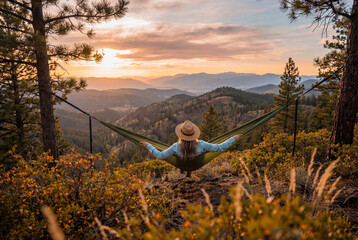 Fototapeta premium Woman relaxing in a green hammock suspended between trees overlooking mountains at sunset