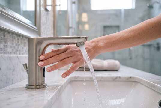 Female hands activating touchless faucet with water flow