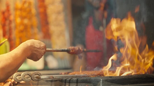 Ramadan street food stall with rows of marinated chicken kebabs hanging on skewers while a vendor grills meat over intense charcoal flames at a busy night market.