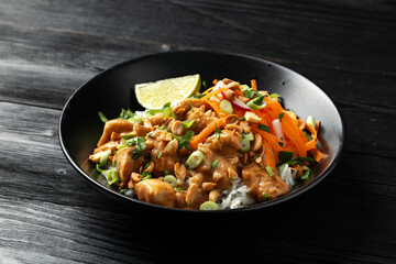 Chicken Satay with rice, roasted peanuts and greens in a black bowl