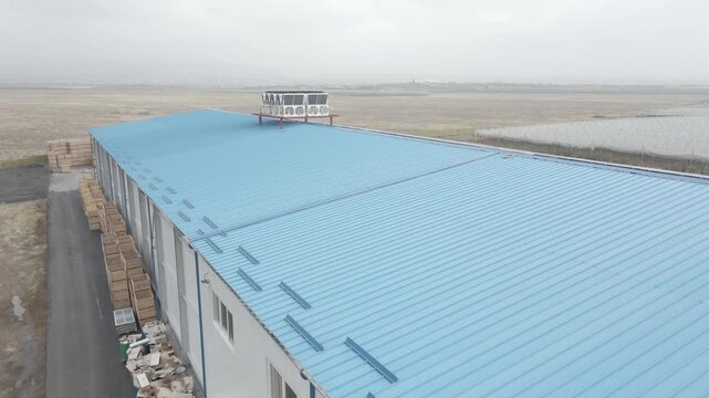 Aerial view of a large agricultural warehouse with a blue roof covered in solar panels. A forklift moves crates while a loaded truck arrives with fresh farm produce.

