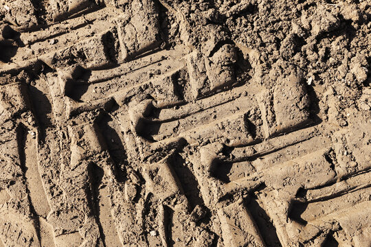 Closeup of tire tread marks in sandy soil. Vehicle track pattern impressed in dry dirt ground. Off road wheel imprint texture creating rugged natural background.