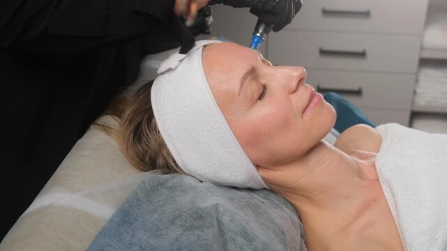 Cosmetologist performing a microneedling anti-aging therapy on a woman's face in a beauty salon