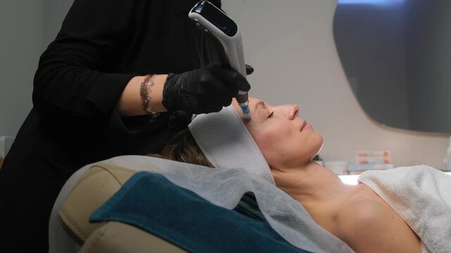 Beautician performs fractional mesotherapy for a female client in a modern cosmetology clinic
