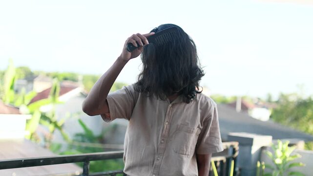 Young Asian Man with Long Hair Combing His Mane Outdoors. Man Combing Long Hair