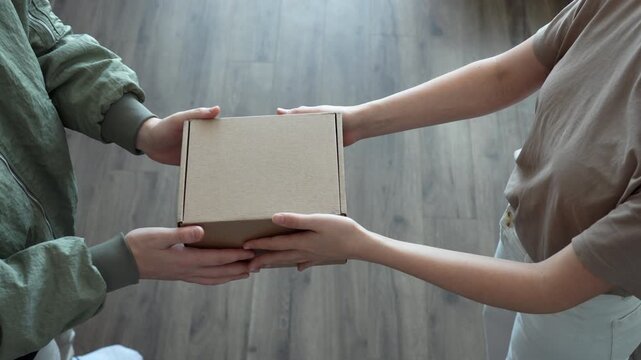 Close up overhead shot capture two individuals engage in a transfer of a small cardboard box. One person hands over the item while the other receives it, delivery, shipping, or receivin- 4k video