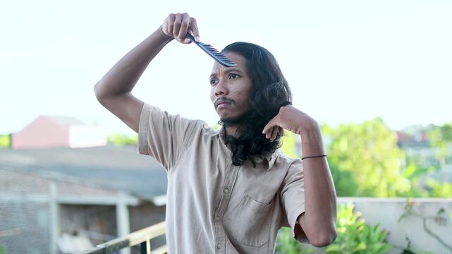 Bearded Male Character Styling His Trendy Long Hair on a Balcony. Man Combing Long Hair