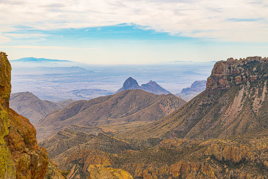 Iconic pyramid-shaped peaks of the Chisos Mountains rise dramatically from the desert floor at Big Bend National Park. Golden-brown rocky terrain contrasts with blue atmospheric haze in distant ridges