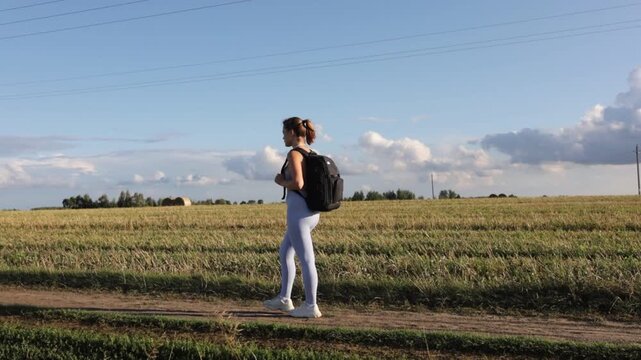 A woman with a backpack in sportswear walks through a field on a bright sunny day on a hike