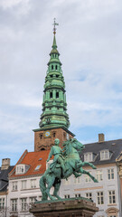 Obraz premium Absalon's statue stands in Hojbro Plads, Copenhagen with a tall spire in the background. The statue commemorates the city's founder, marking his historical significance in Denmark.