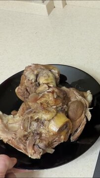 Close-up of cooked pork knuckle on black plate in home kitchen, vertical food video showing traditional boiled pork shank with bone, tender meat and rustic texture ready to serve