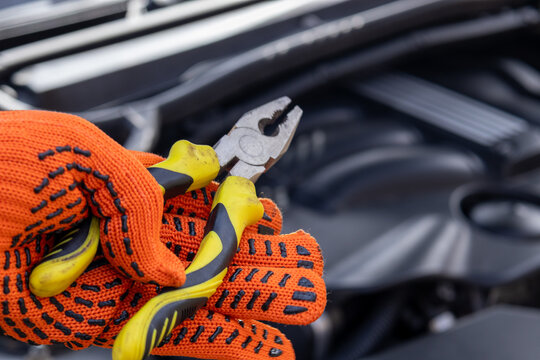 Brightly gloved hands grip pliers as a mechanic focuses intently on engine components, ensuring everything runs smoothly