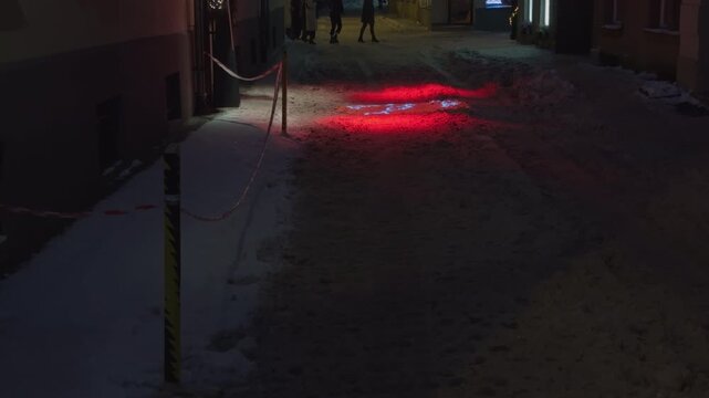 Nighttime urban scene. Snowy alley with neon reflections. Quiet snowy pathway illuminated by colorful neon lights and wet footprints